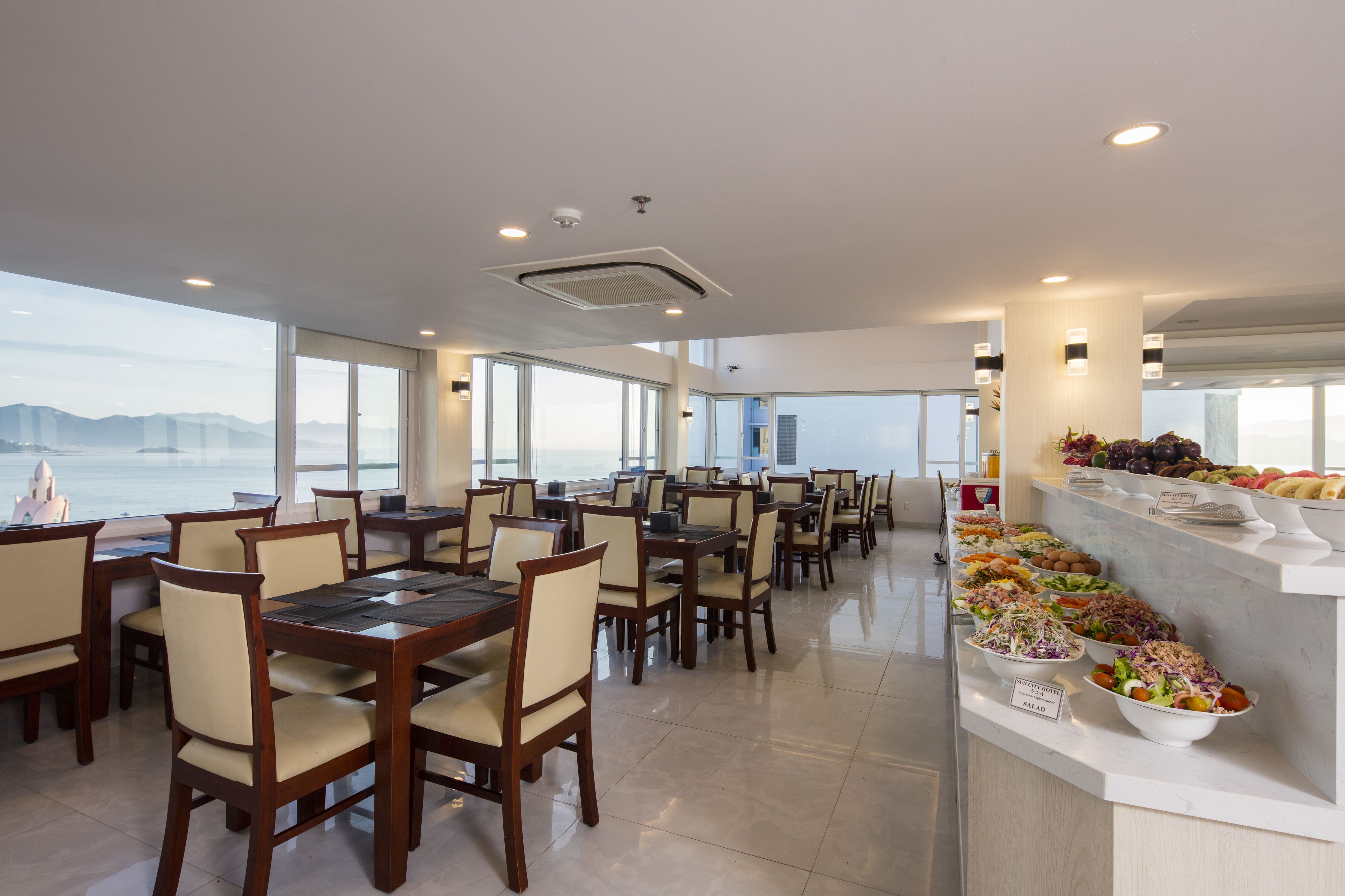 Un comedor con mesas y sillas, un bufé con diversos platos, y vista al mar.