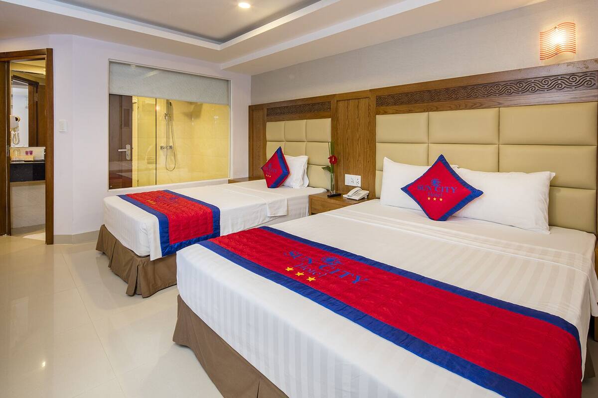 A hotel room with two beds, each with a red and blue bedspread, a wooden headboard, and a mirror above the beds.