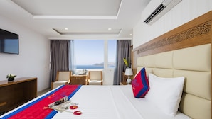 Habitación de hotel con una cama grande, un escritorio, una silla, un televisor y vistas al mar.