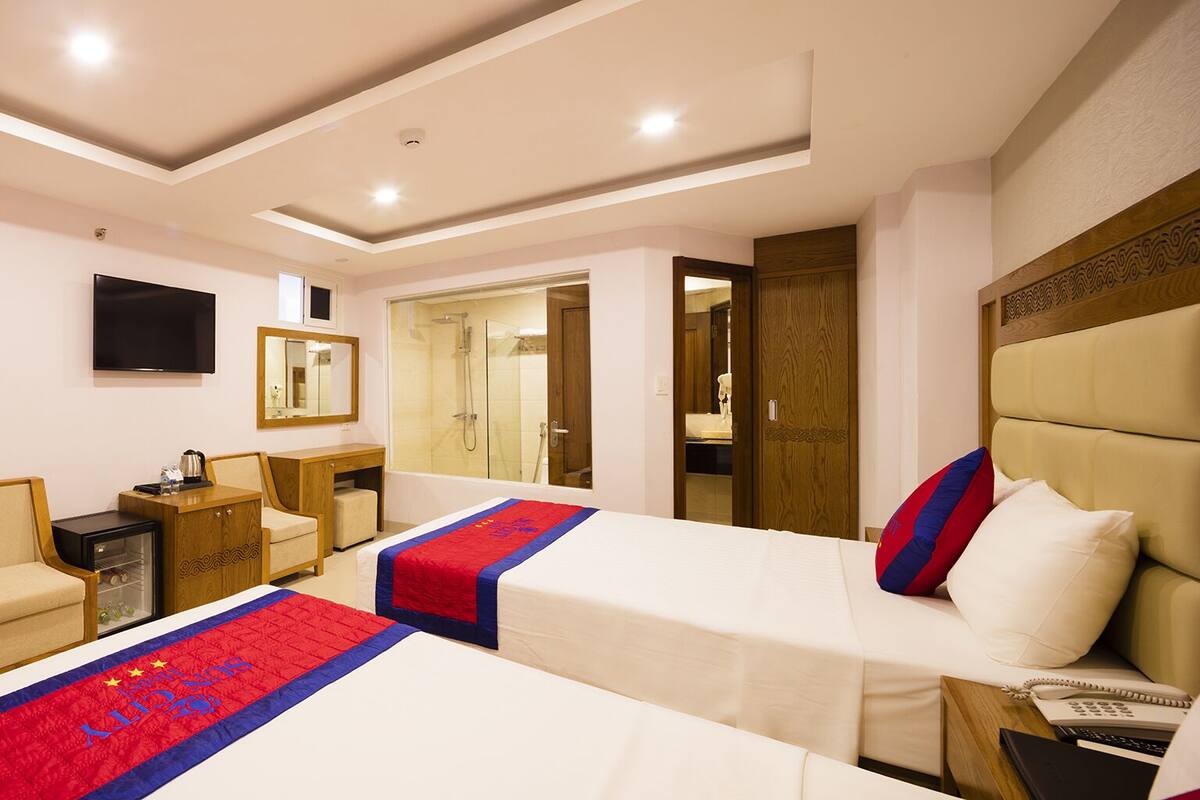 A hotel room with two beds, a TV, a desk, a mirror, and a shower area.