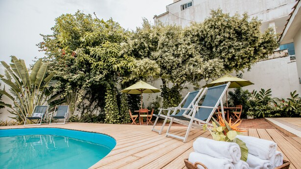 Una terraza de madera con piscina, sillas de descanso y una cesta de mimbre con toallas.