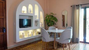 Una habitación moderna con un televisor instalado en una pared blanca, una mesa de comedor con sillas, una planta en maceta y un espejo grande.