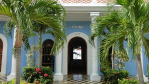 Entrada de un edificio con suelo a cuadros, palmeras y un letrero que dice "Casa Bustamante".