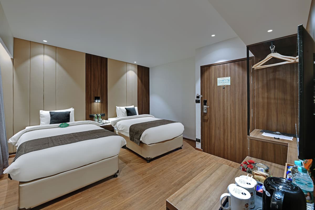 A hotel room with two beds, a wooden floor, a desk with a coffee maker, and a wardrobe.