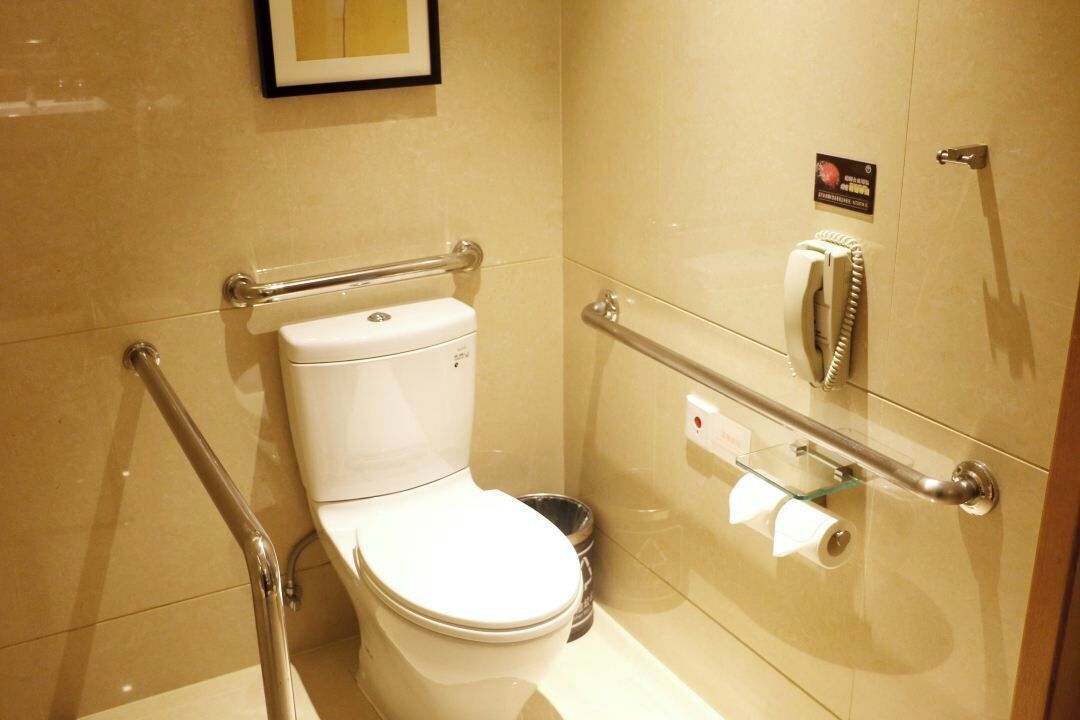 Ein Badezimmer mit Toilette, Handläufe, einer Glasabtrennung und einem Telefon.