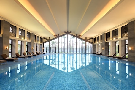 A large indoor swimming pool with lounge chairs and large windows.