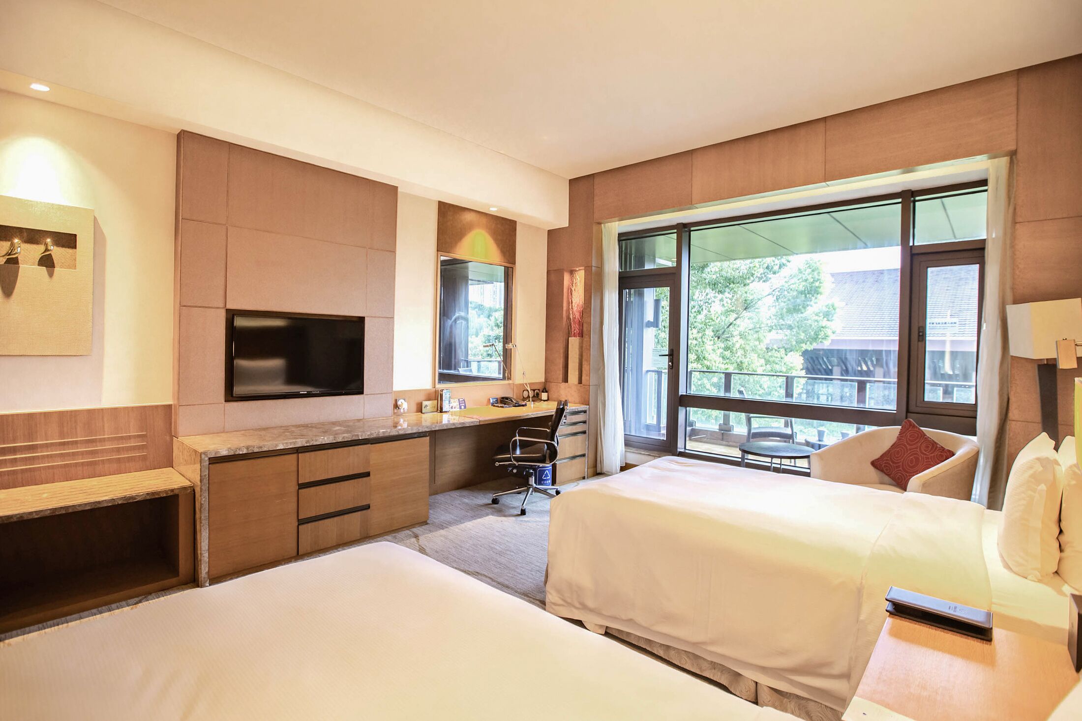Habitación de hotel con dos camas, un escritorio, un televisor y ventanas amplias.