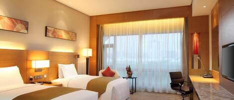 A hotel room with two beds, a desk, a chair, and a large window with curtains.