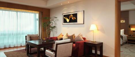 A modern hotel room with a dining area, a sofa set, a coffee table, a lamp, and a painting on the wall.