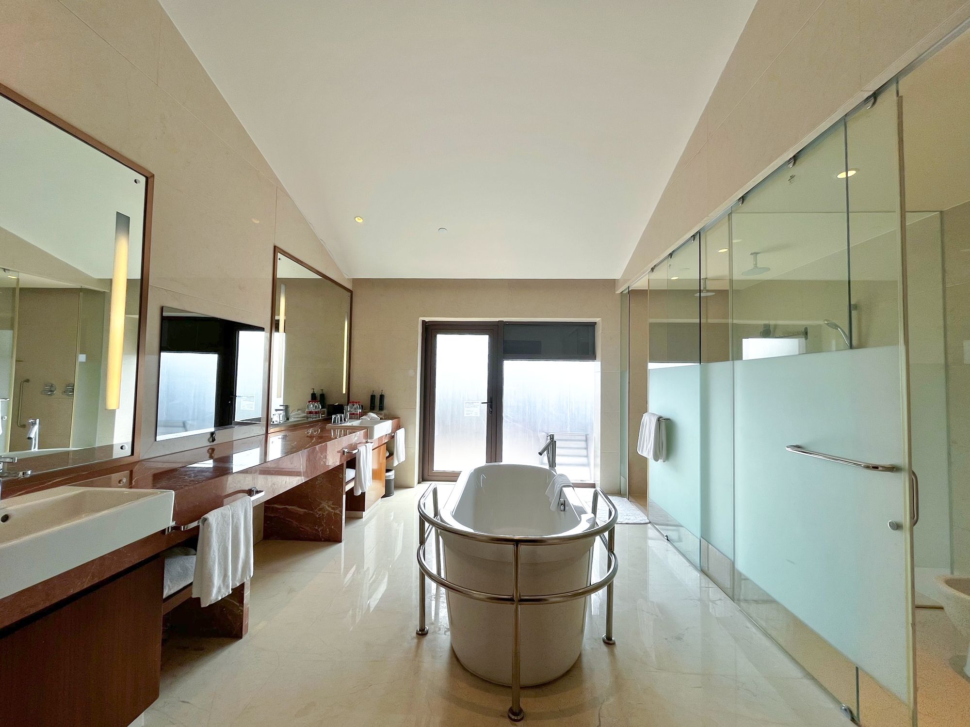 Un baño moderno con un espejo grande, una bañera y una zona de ducha con paredes de vidrio.