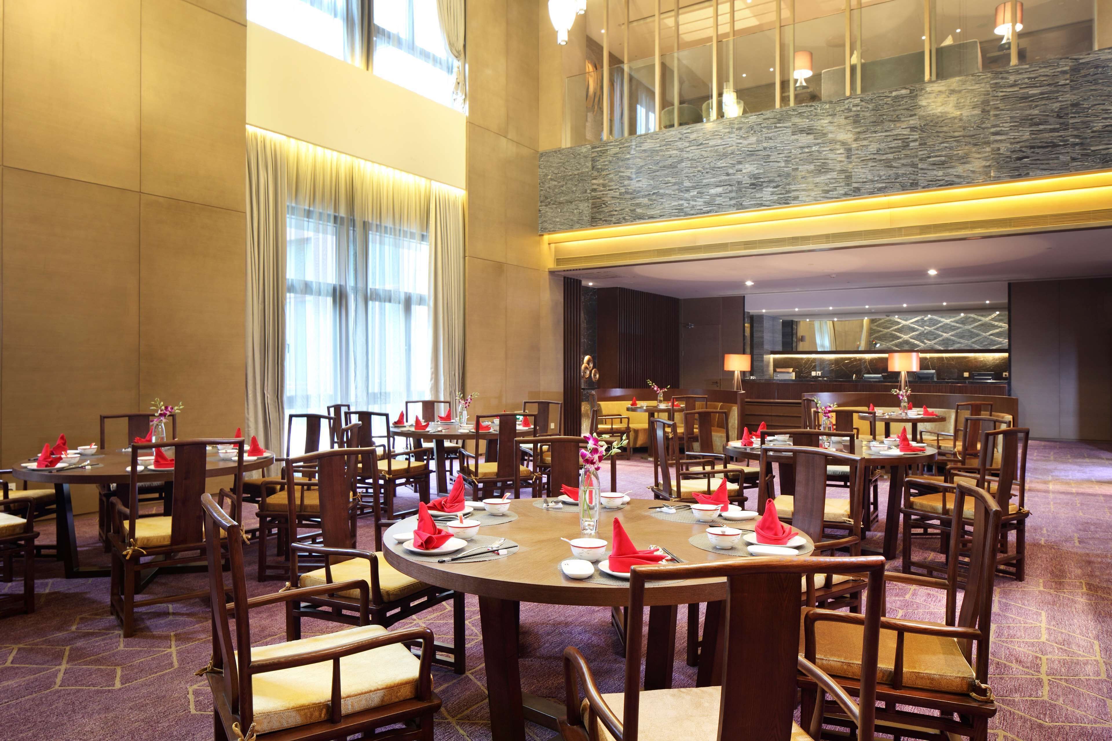 Une salle à manger d’hôtel avec plusieurs tables rondes, des chaises en bois et un plafond haut agrémenté d’un mur en pierre.