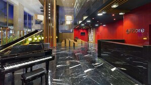 A grand piano in a spacious lobby with a polished marble floor, a reception desk, and a red accent wall with the Encore logo.