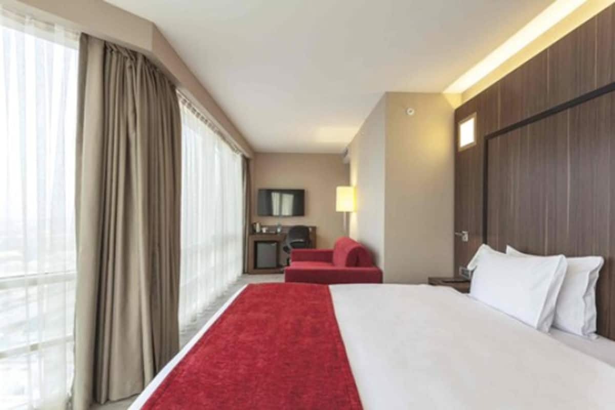 Quarto de hotel com uma cama grande, uma escrivaninha, uma cadeira e uma televisão.