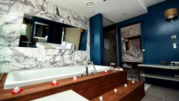 Un baño moderno con pared de mármol, una bañera grande, tocador de madera y un espejo.