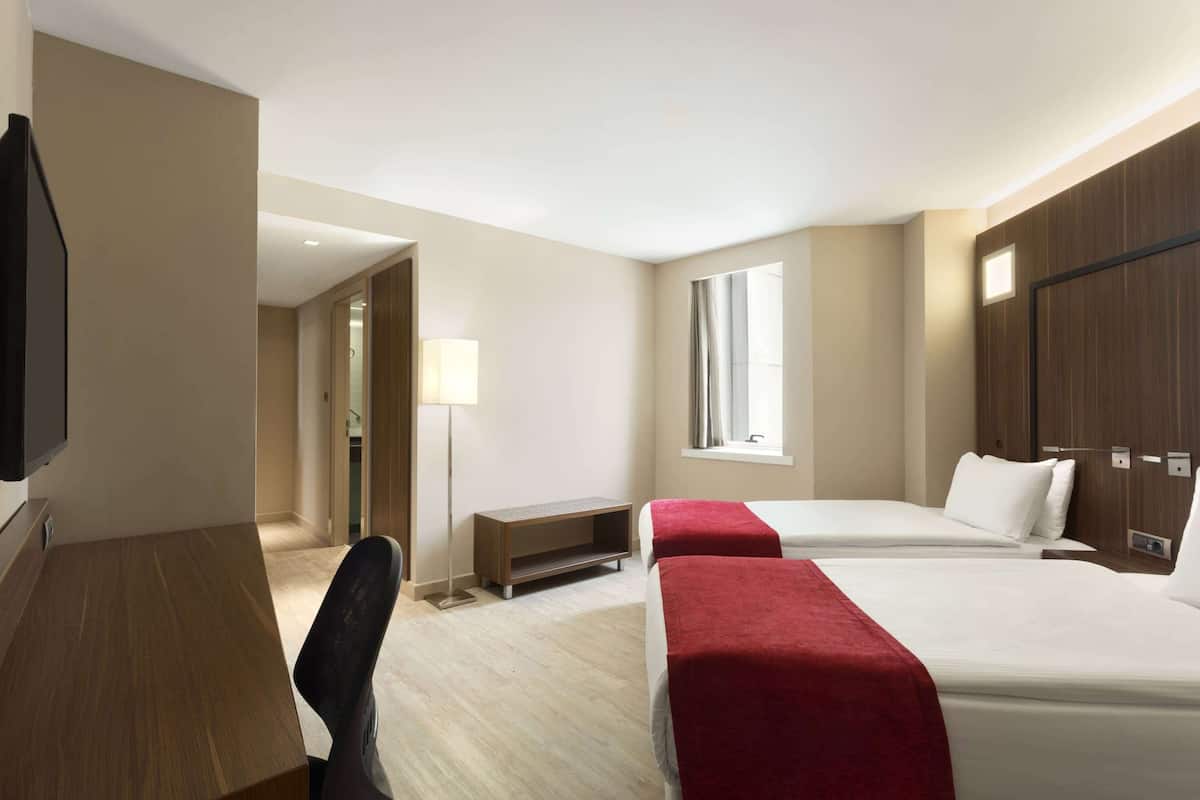 Quarto de hotel com duas camas, uma escrivaninha, televisão e janela.