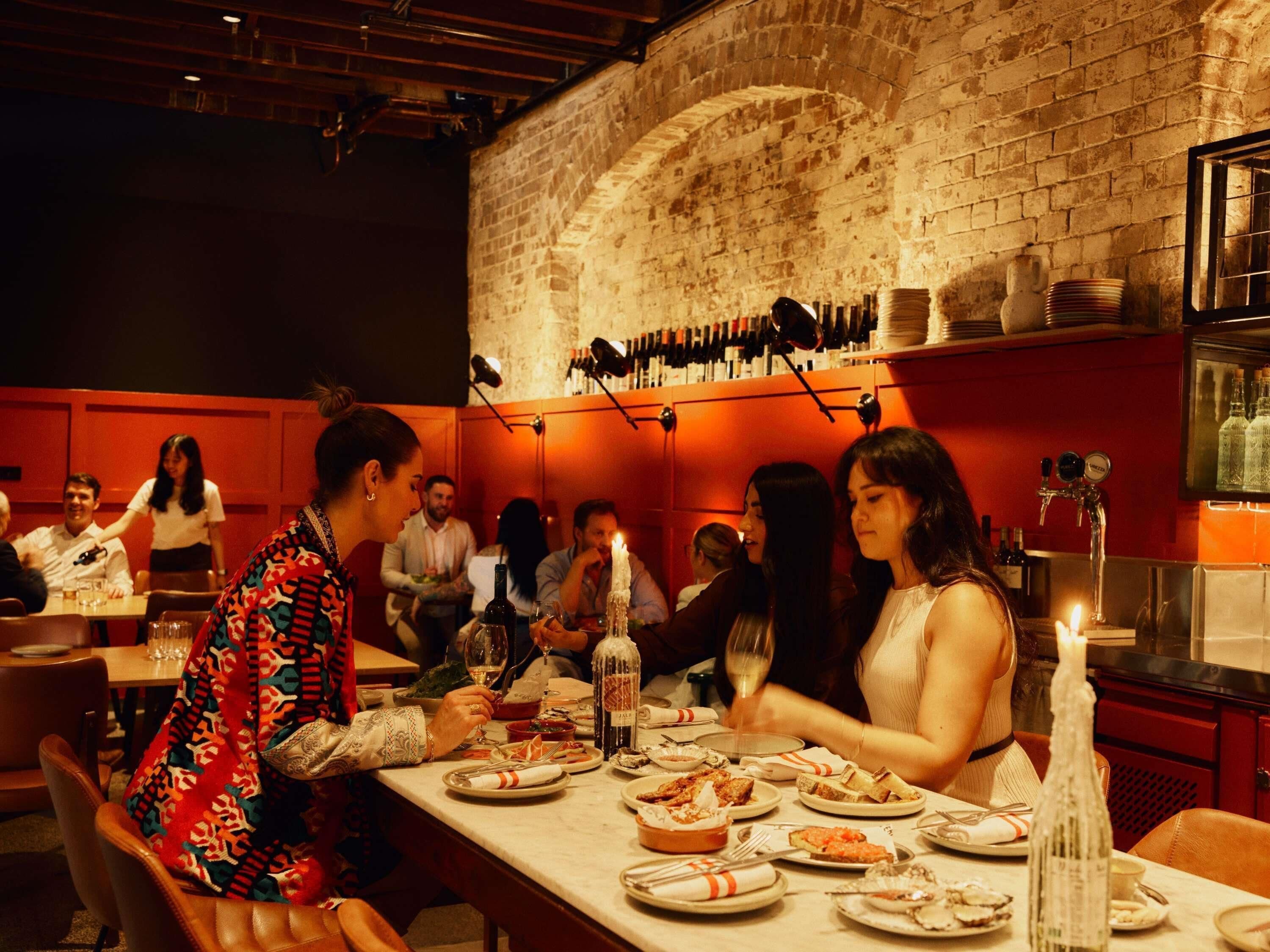 A restaurant with brick walls, tables set with plates and glasses, and bottles on the wall.