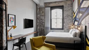 A bedroom with a bed, a desk, a chair, a TV, and a window with a view.