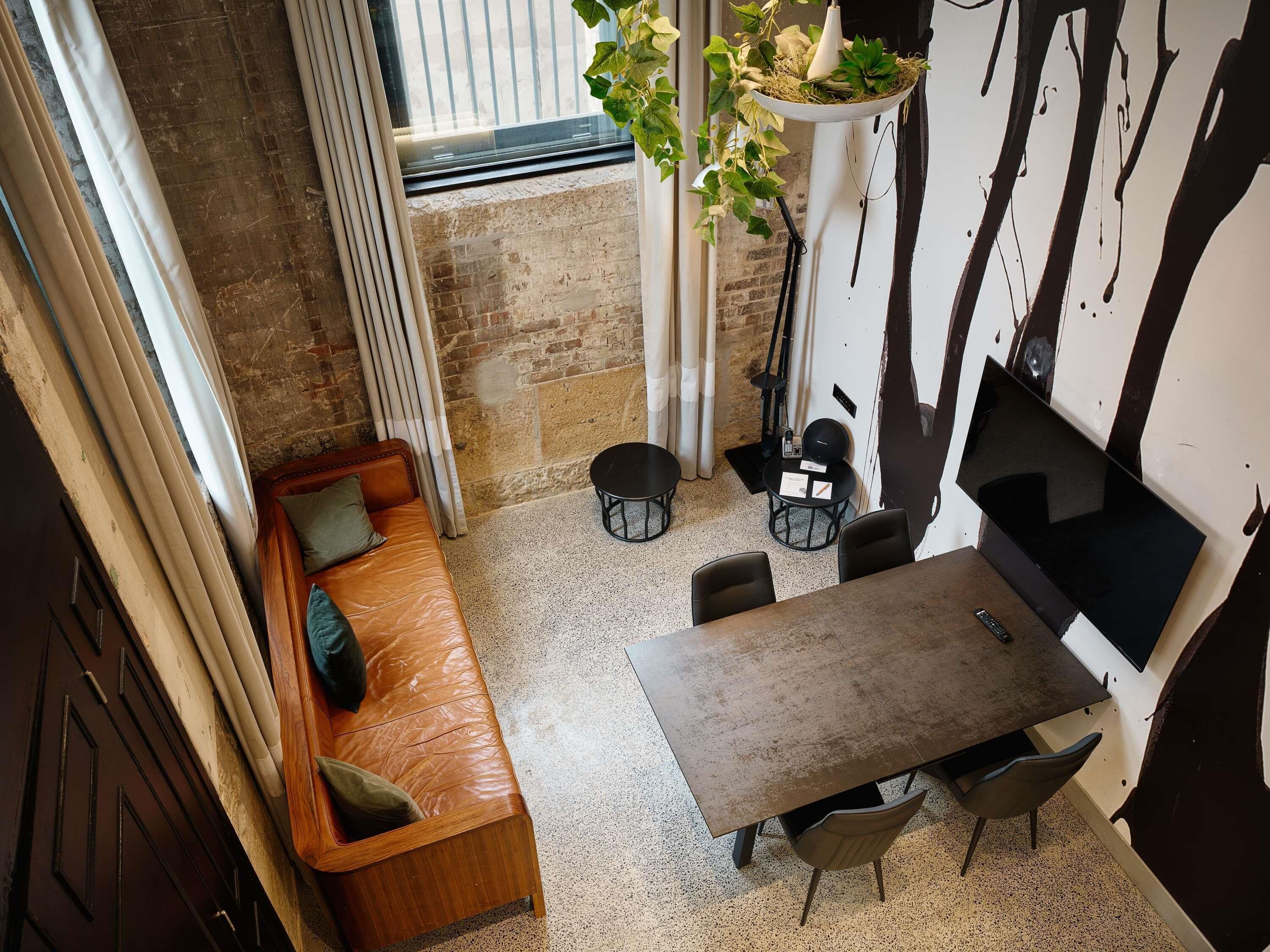 A cozy room with a brown leather sofa, a small round table, and chairs, a potted plant, and a TV mounted on the wall.