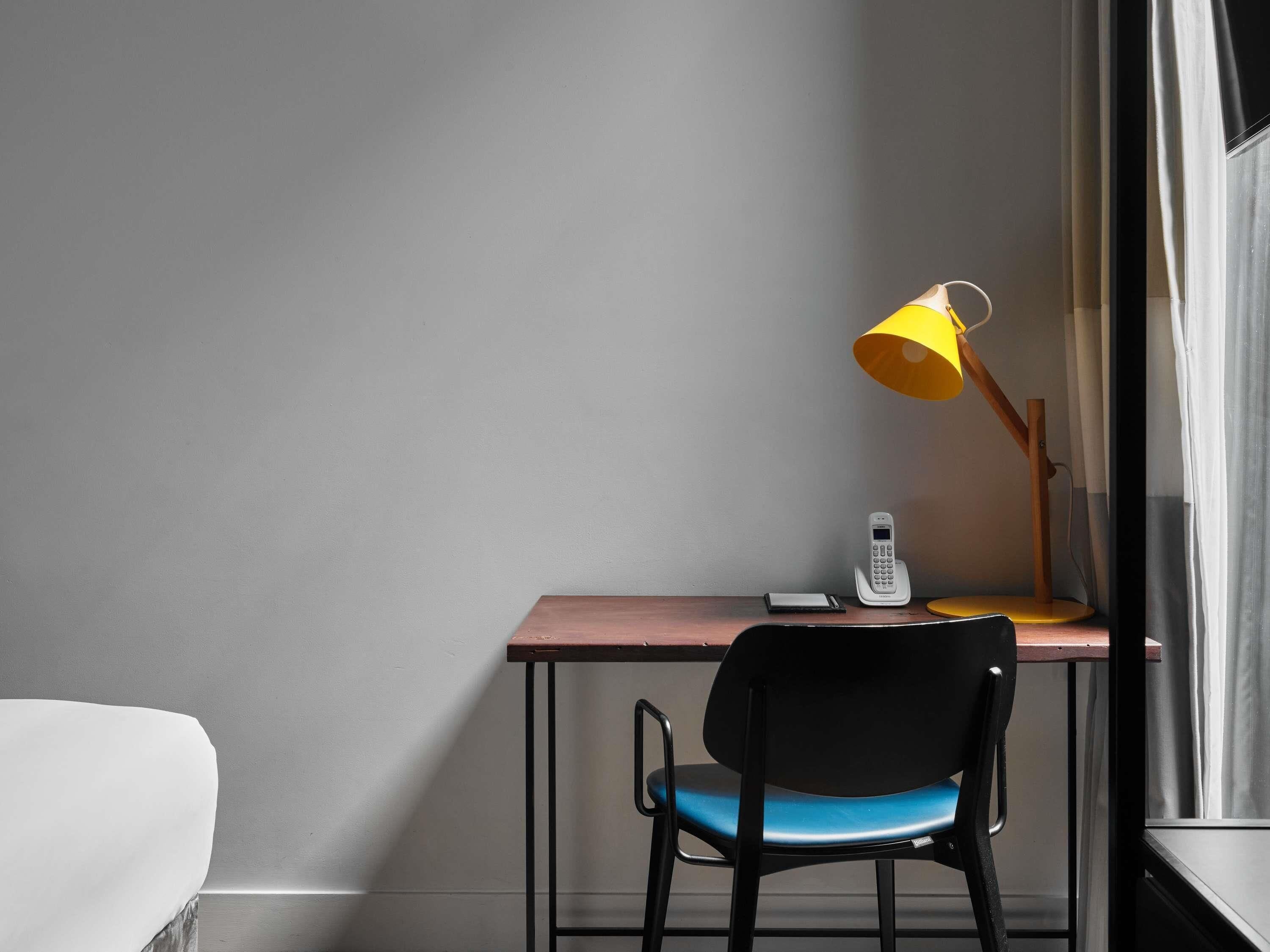 Un escritorio con un teléfono, una lámpara y una silla en una habitación con ventana.