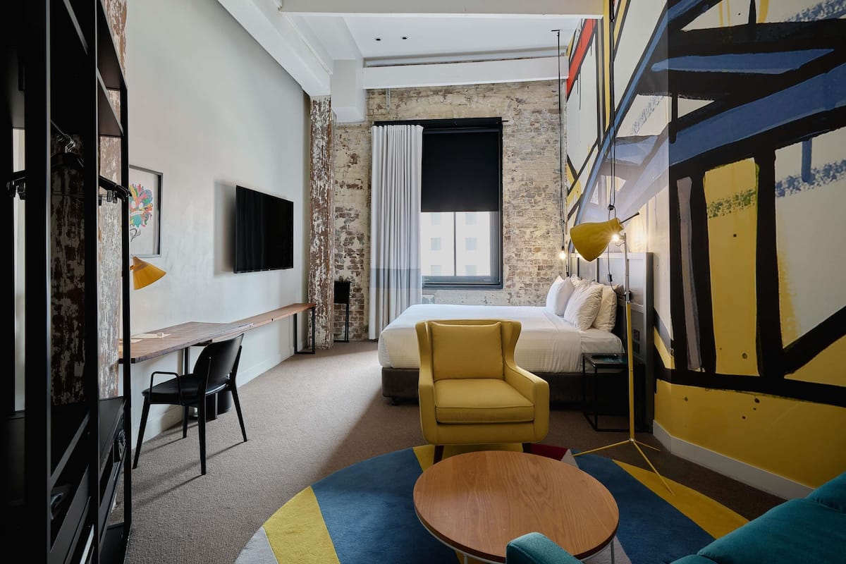 Una habitación de hotel moderna con una cama, un escritorio, una silla, una mesa redonda y un televisor.
