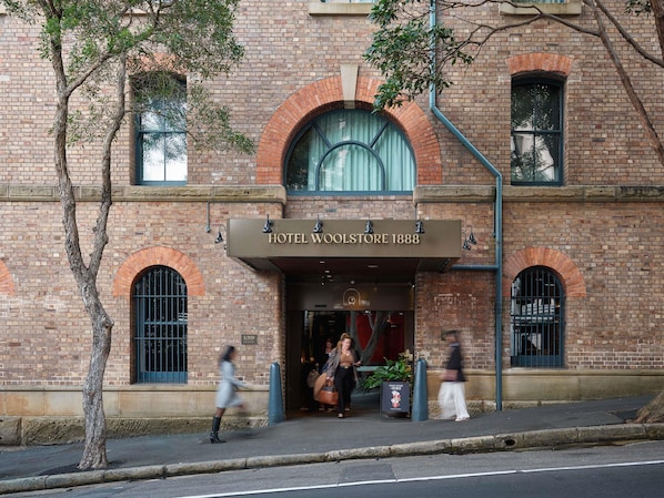 Ein historisches Gebäude mit einem markanten Bogenportal und einem Schild, auf dem 'HOTEL WOOLSTORE 1888' steht.