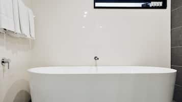 A modern bathroom with a freestanding bathtub, a towel rack with folded towels, and a wall-mounted control panel.