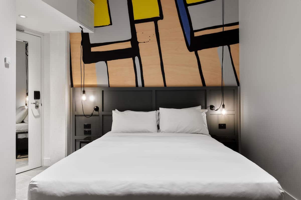 Un dormitorio moderno con una cama grande, cabecera con arte mural geométrico, lámparas de noche y una puerta con interruptor de luz.