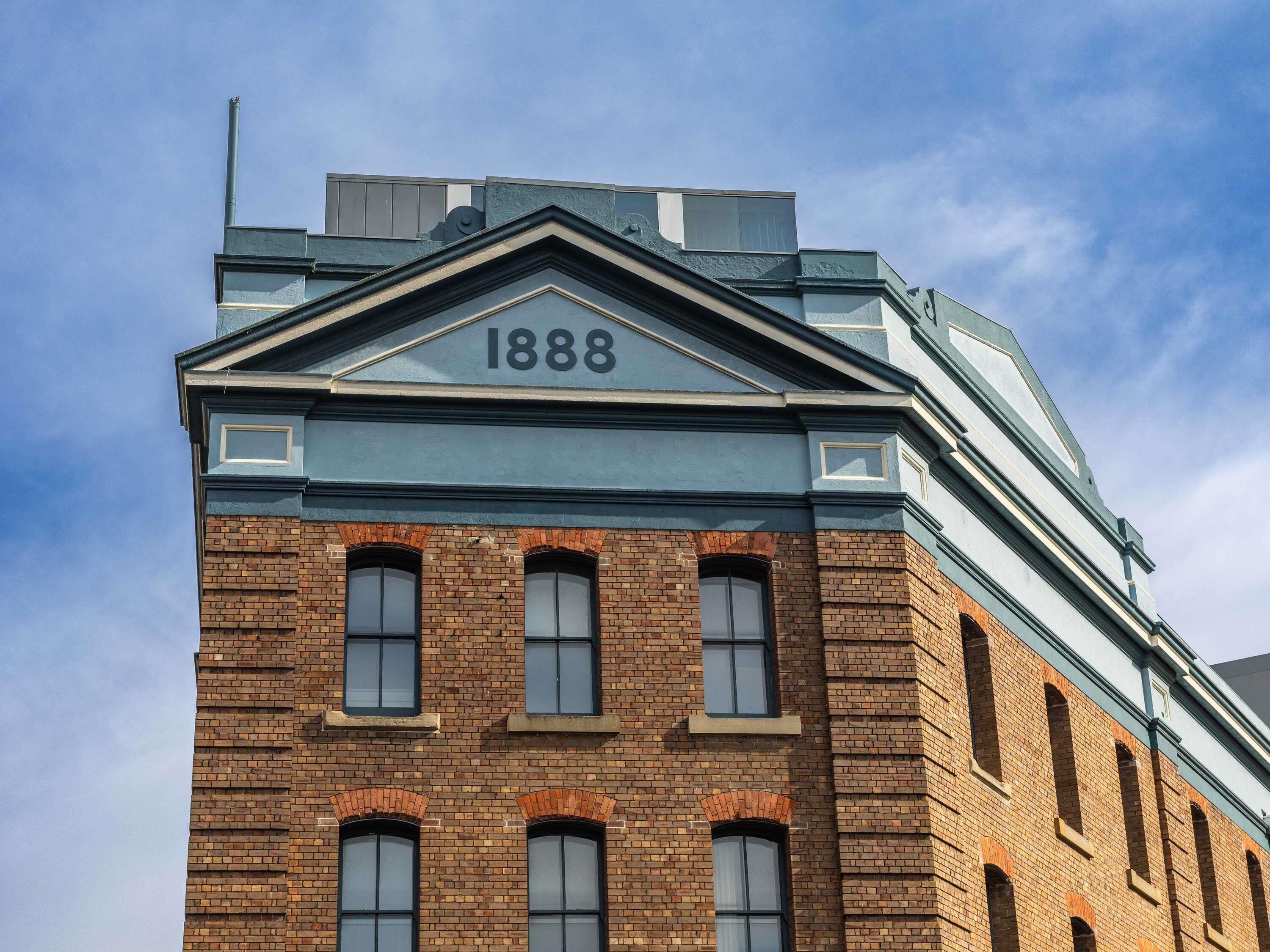 Un edificio de ladrillo con el número 1888 en la fachada, ventanas amplias y techo plano.