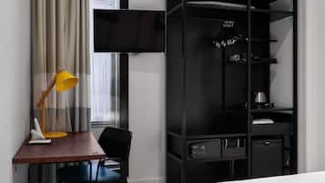 Habitación de hotel con cama, escritorio, silla, armario negro, televisor y ventana con cortinas.