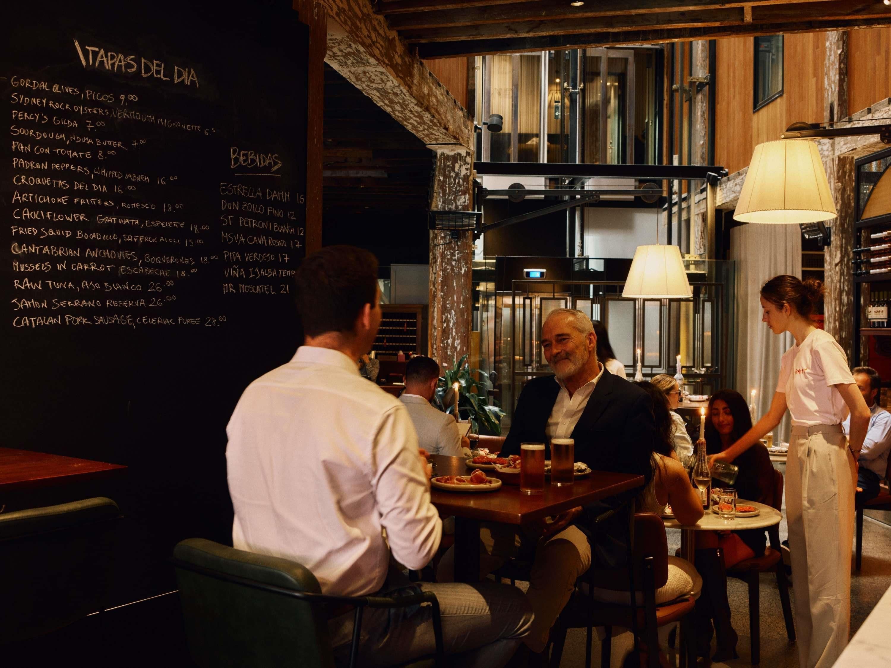 A restaurant interior with a menu on the wall, wooden beams, and a bar area.