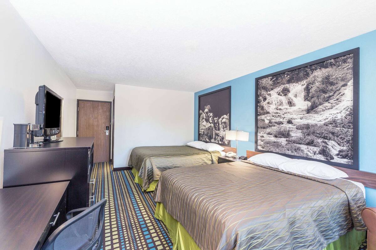 A hotel room with two beds, a desk with a chair, a television, and a large framed picture on the wall.