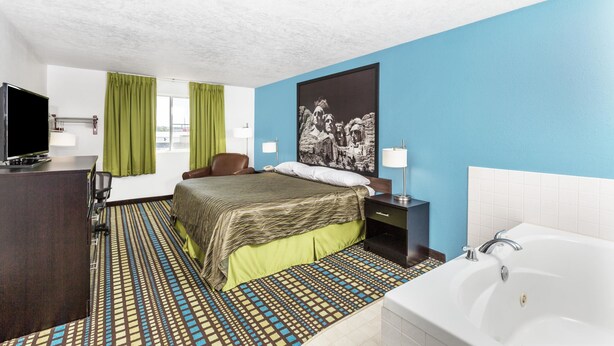 A hotel room with a bed, a desk with a TV, a bathroom with a bathtub, and a large window with curtains.