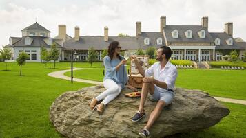 Two people sitting on a rock in a grassy area with a large house in the background.