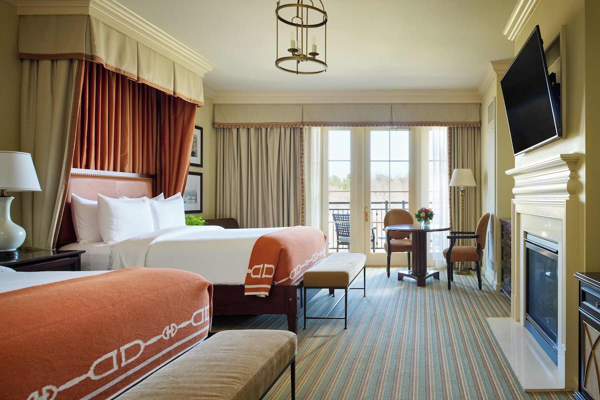 A hotel room with two beds, a dining table, chairs, a fireplace, and a TV.