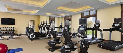 Une salle de sport équipée de tapis de course, de vélos elliptiques et d’une zone avec des bancs de musculation.