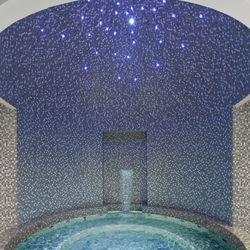 A hot tub with a mosaic ceiling and walls, surrounded by a tiled floor.