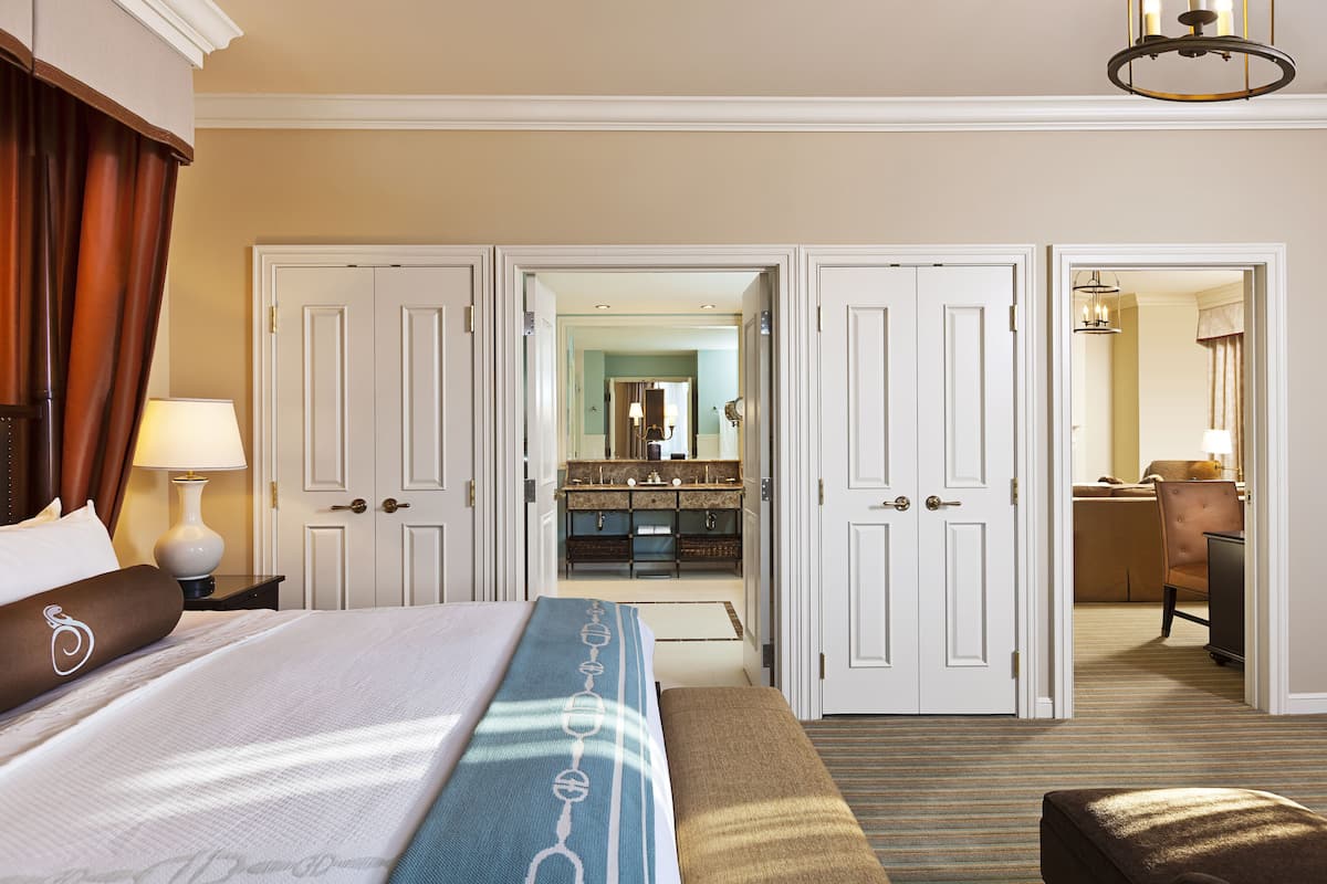 A hotel room with a large bed, a desk, a chair, and a bathroom visible through an open door.