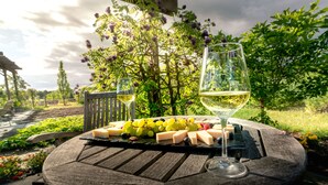 A picnic setup with a cheese board, grapes, and a glass of white wine on a wooden table, surrounded by lush greenery and a pergola. - Salamander Resort And Spa (Middleburg)