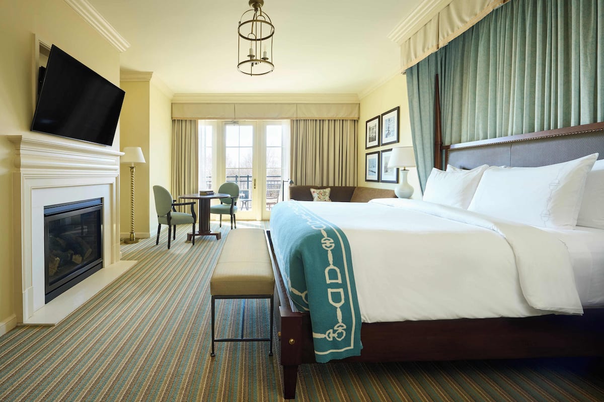 A hotel room with a large bed, a fireplace, a television, a desk, and a balcony view.