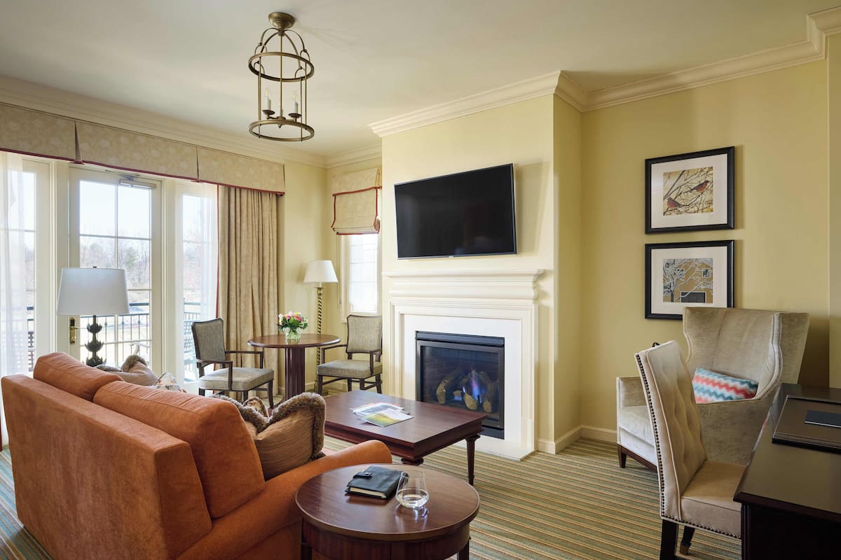 A hotel room with a sofa, armchairs, a fireplace, a television, and framed artwork on the wall.