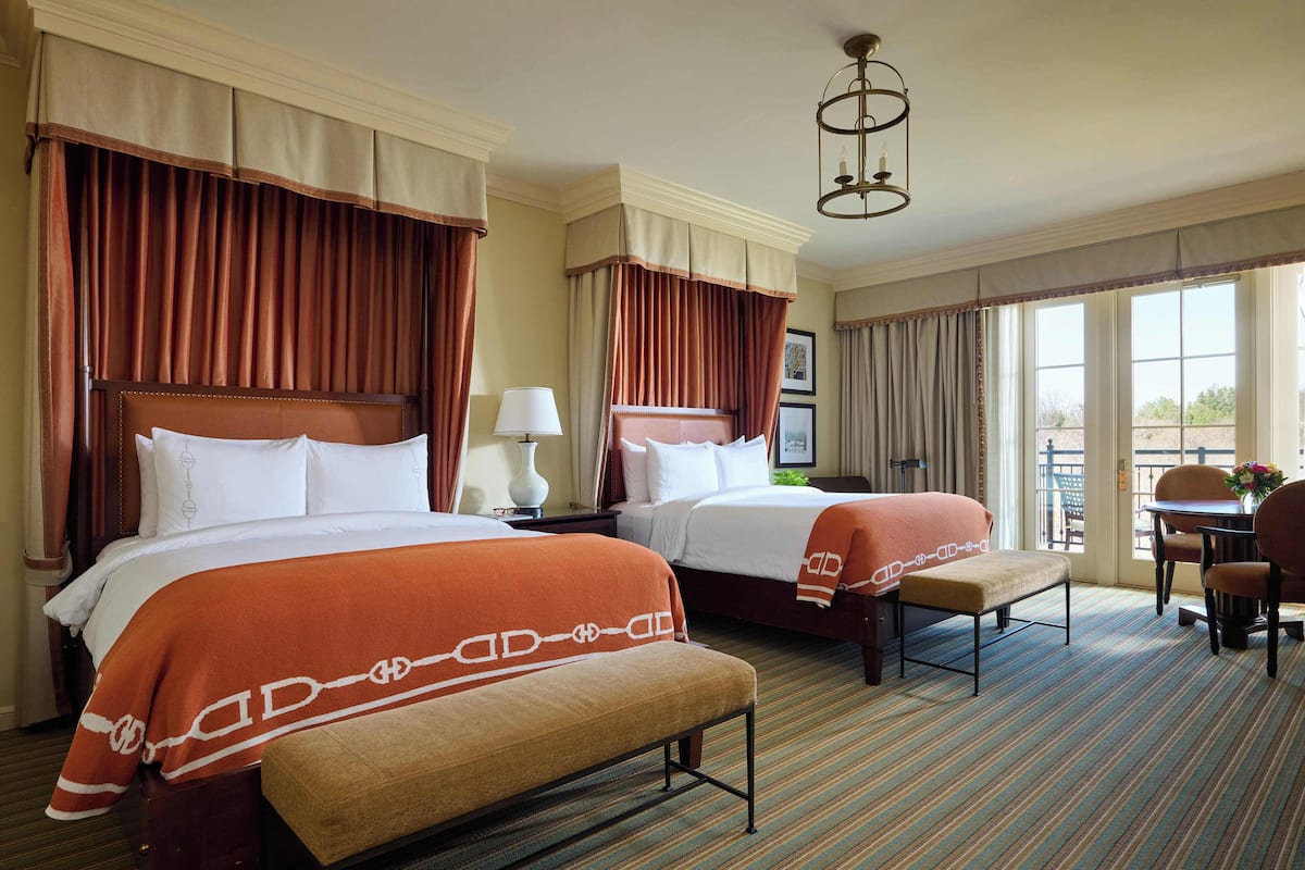 A hotel room with two beds, a bench, a desk, and a chair.