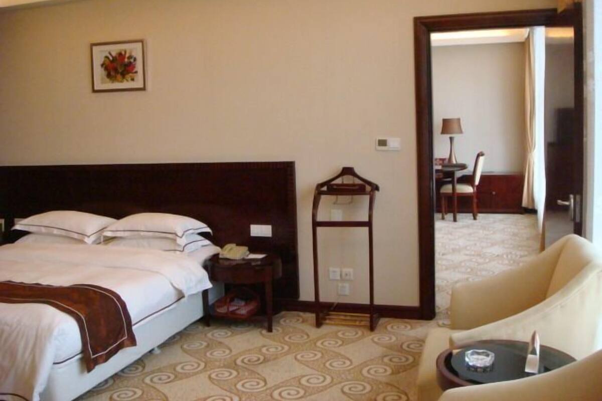 A hotel room with a bed, a bedside table, a chair, a small table, and a mirror.