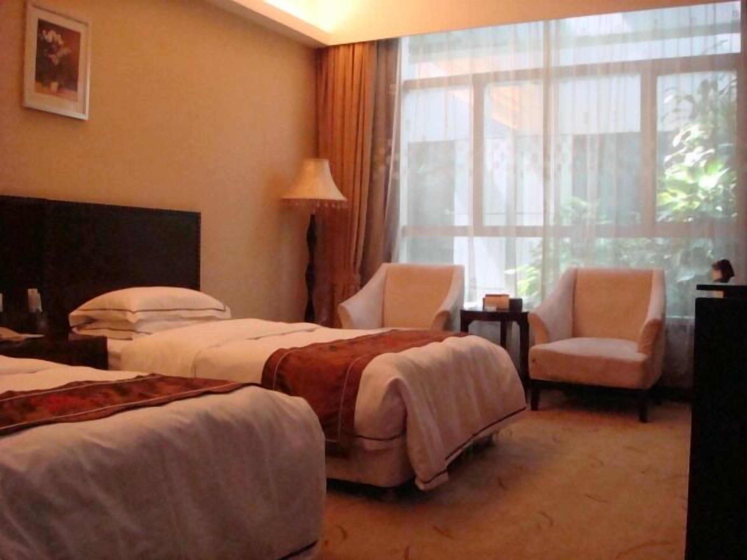 A hotel room with two beds, a sitting area with chairs, a lamp, and a large window with curtains.