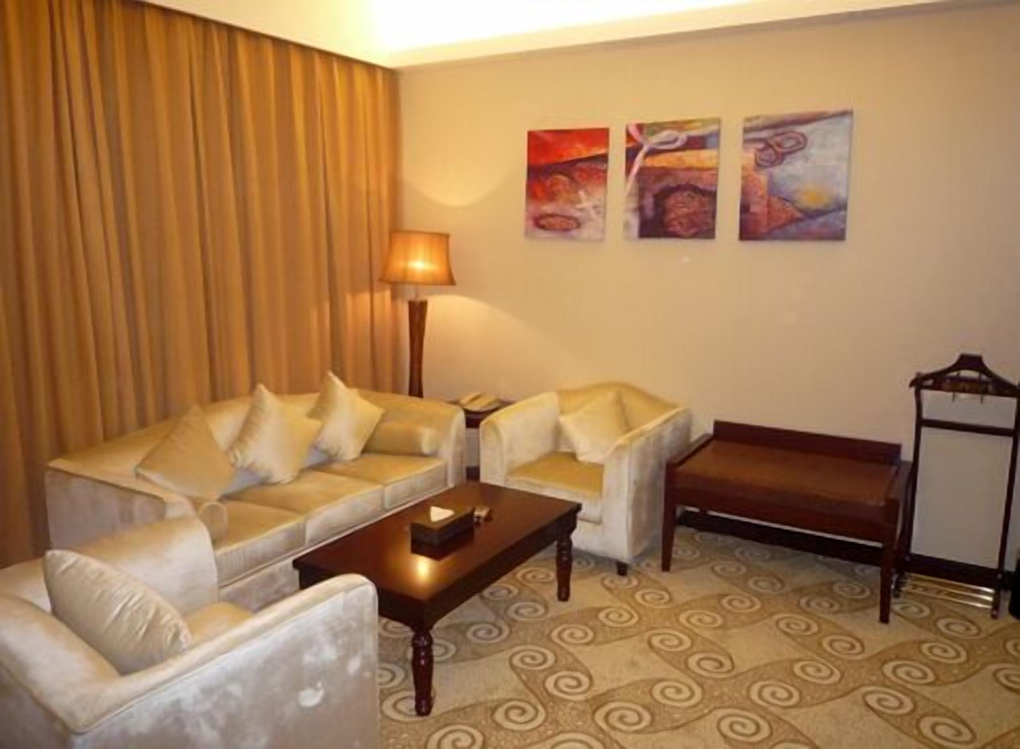 Habitación de hotel con sofá, dos sillones, una mesa de centro, una lámpara y tres cuadros en la pared.