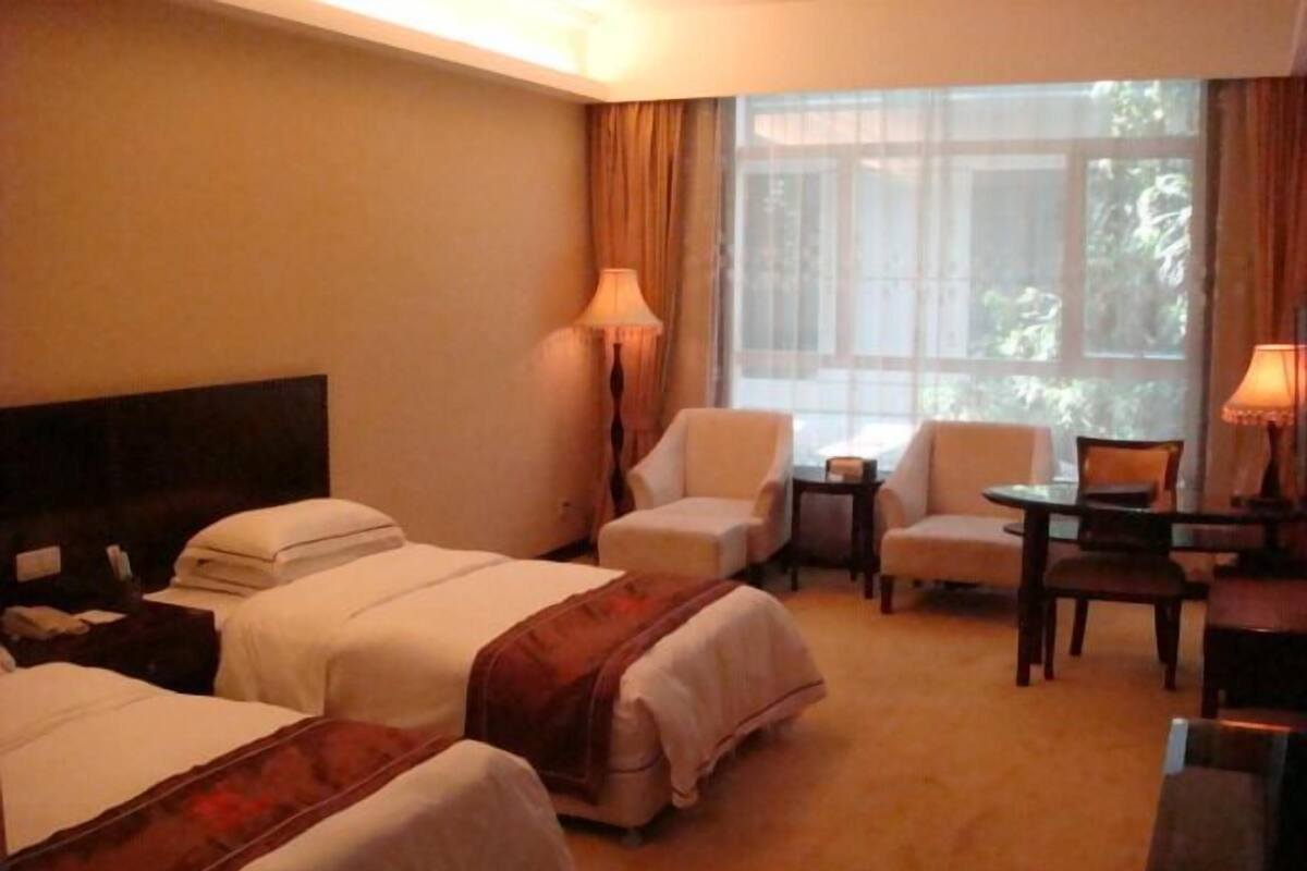 A hotel room with two beds, a desk, a chair, and a window with curtains.