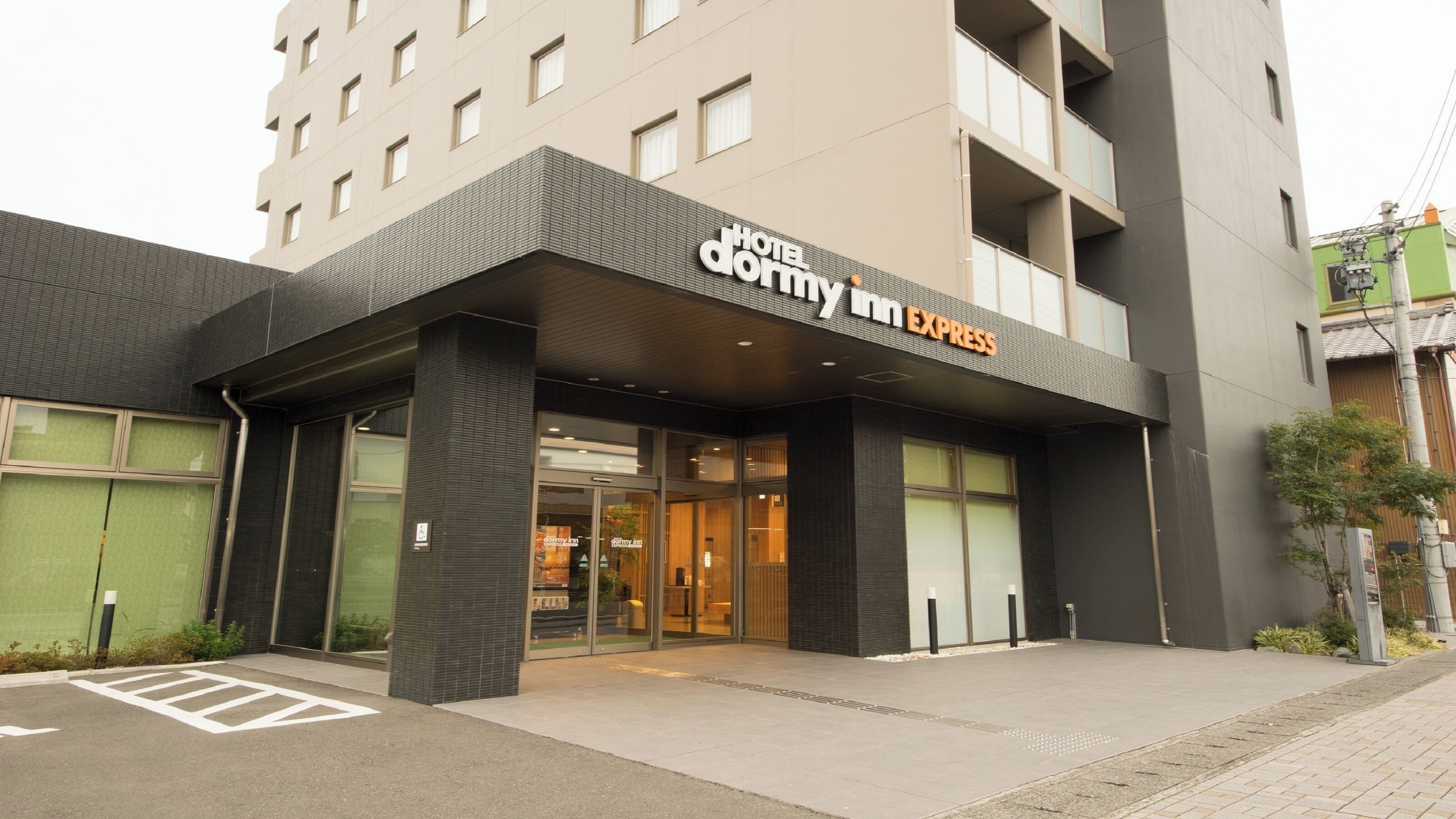 Een hotelentree met een modern ontwerp, met een opvallend bordje voor 'Hotel Dormy Inn Express'.