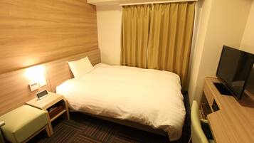 A hotel room with a bed, a desk with a chair, a television, and a small table with a clock.