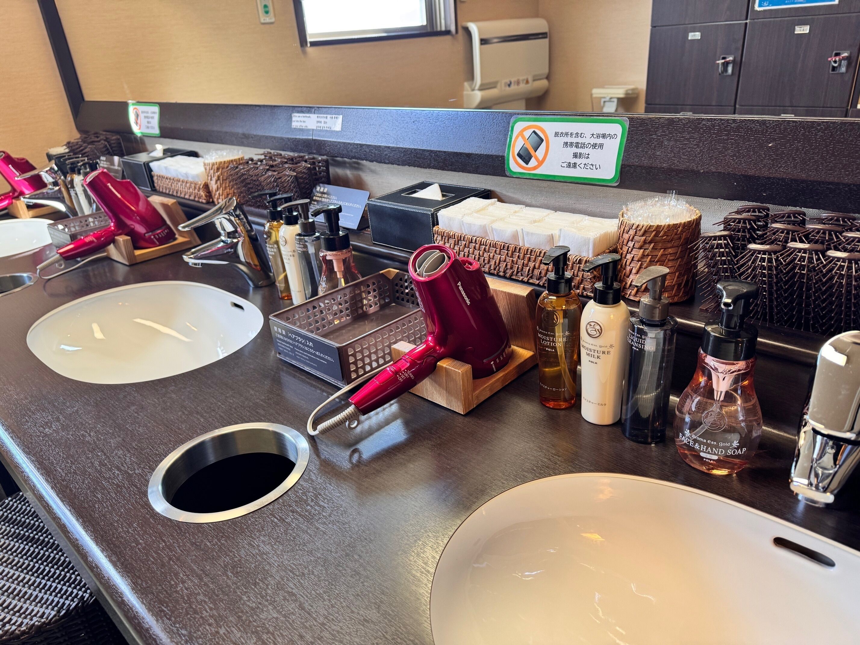 A hotel bathroom with two sinks, a red hairdryer, and various toiletries on the counter.