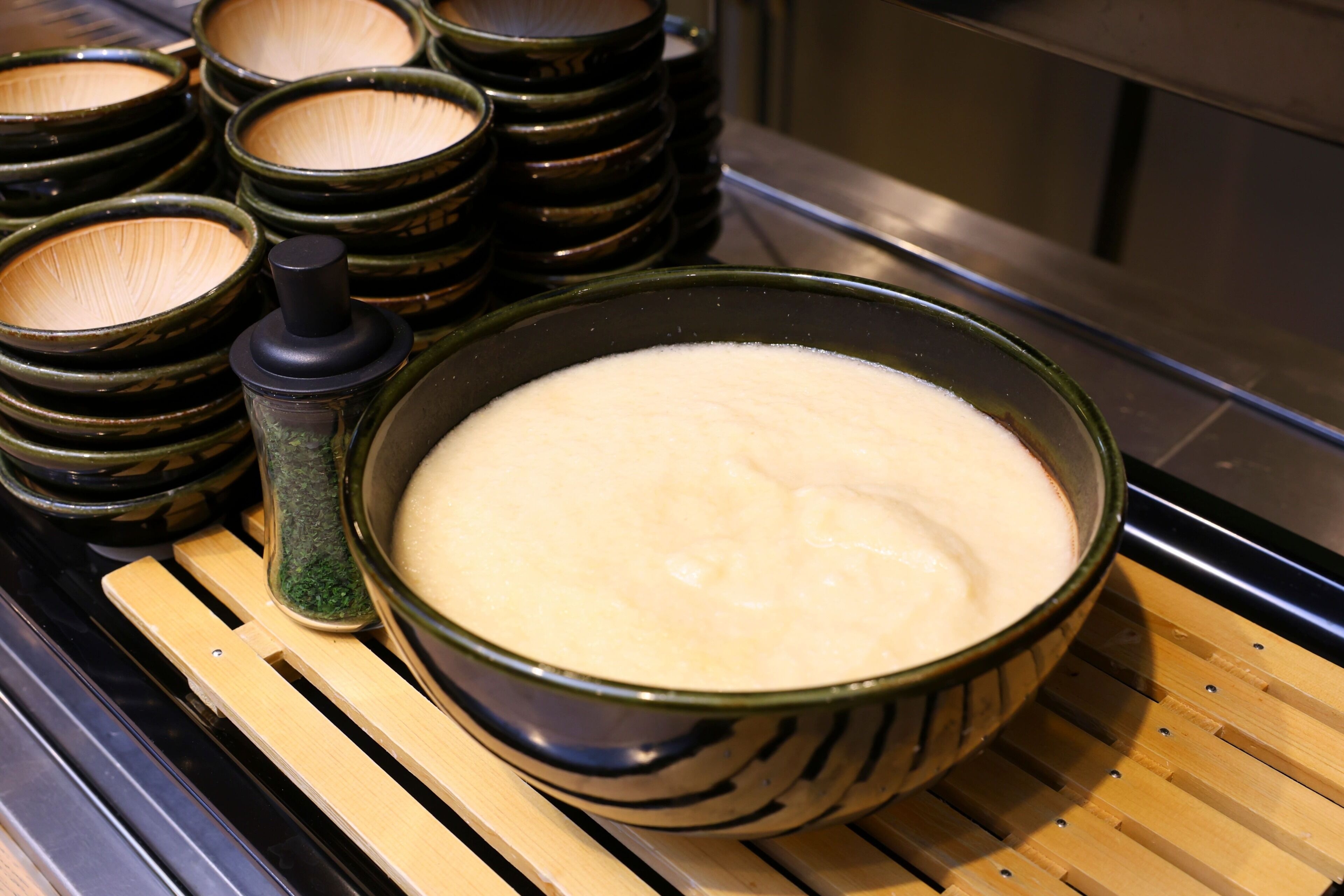 A kitchen with a large pot on a stove, surrounded by several bowls and a spice grinder.