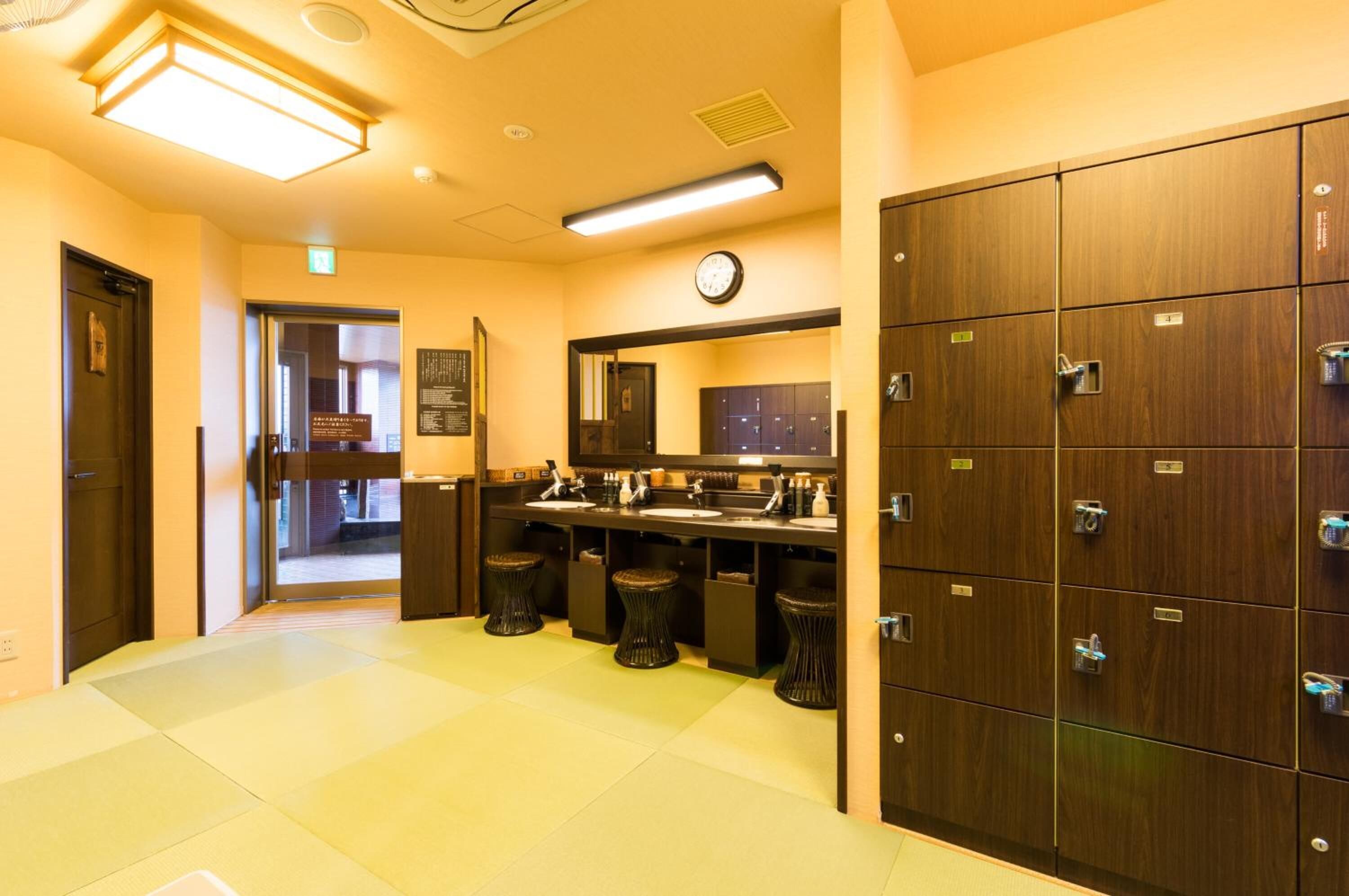 Une salle de bain d’hôtel avec plusieurs casiers, un coin lavabo et une horloge au mur.